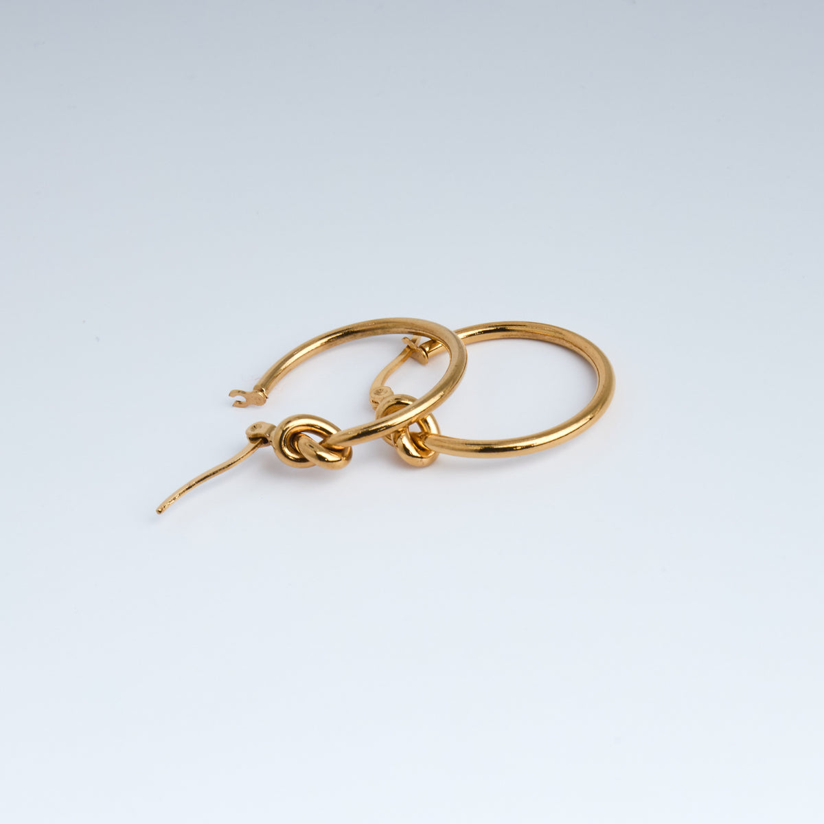 Gold hoop earrings with a knot design on a light gray background