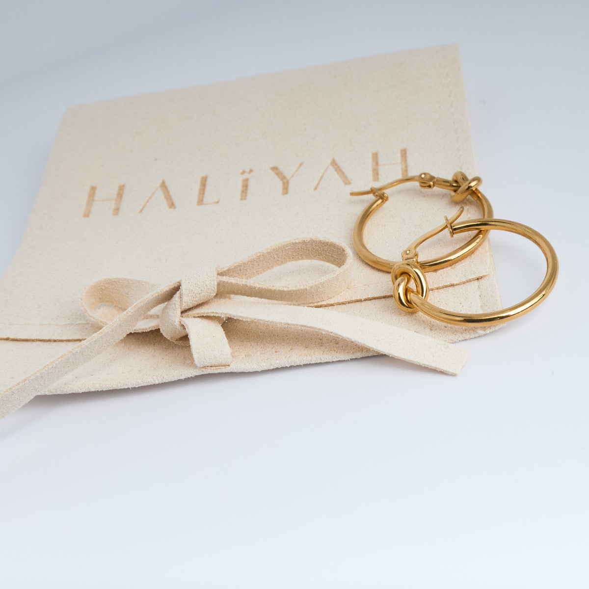 Gold hoop earrings on a beige fabric with 'HALIYAH' branding.
