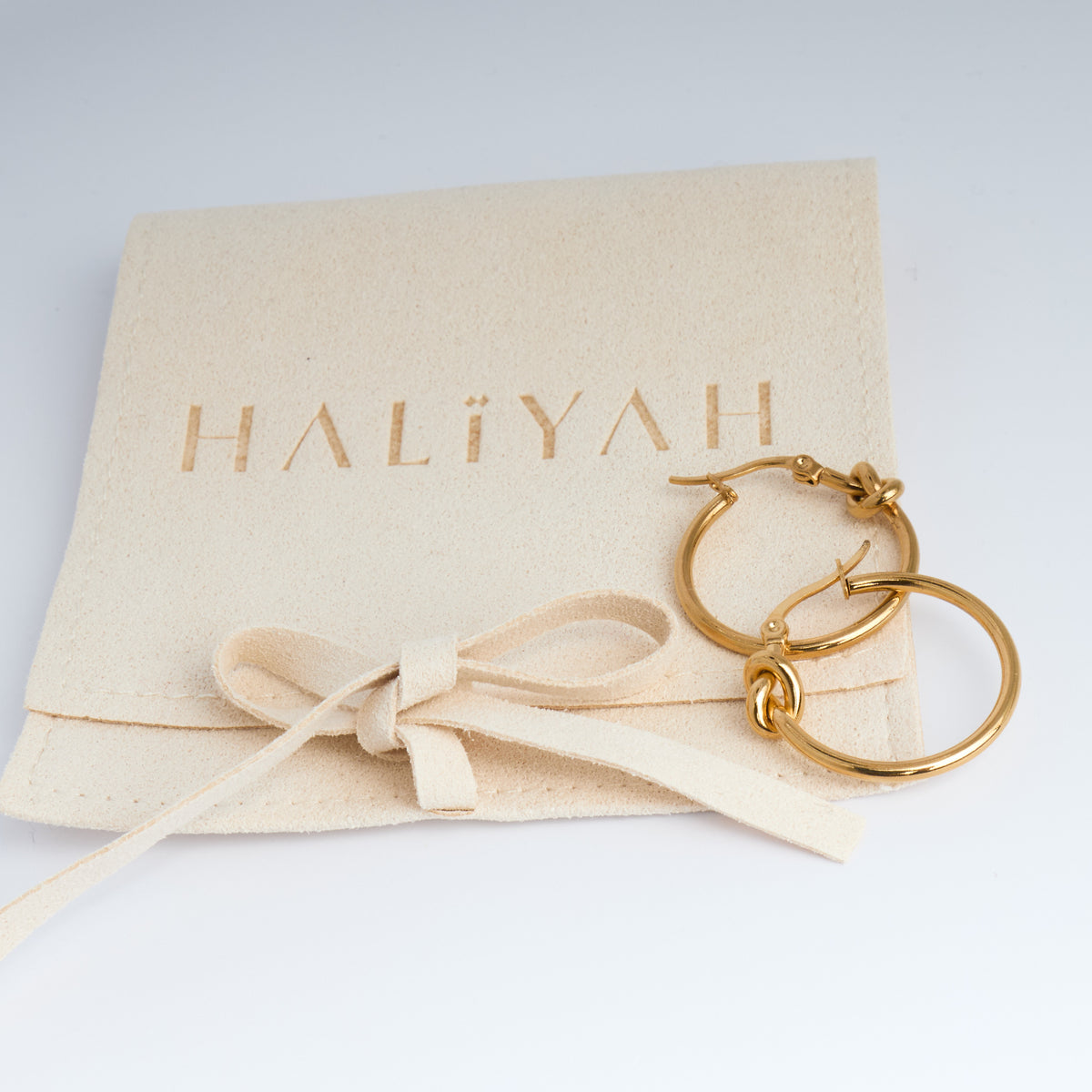 Gold hoop earrings on a beige fabric with 'HALIYAH' branding.