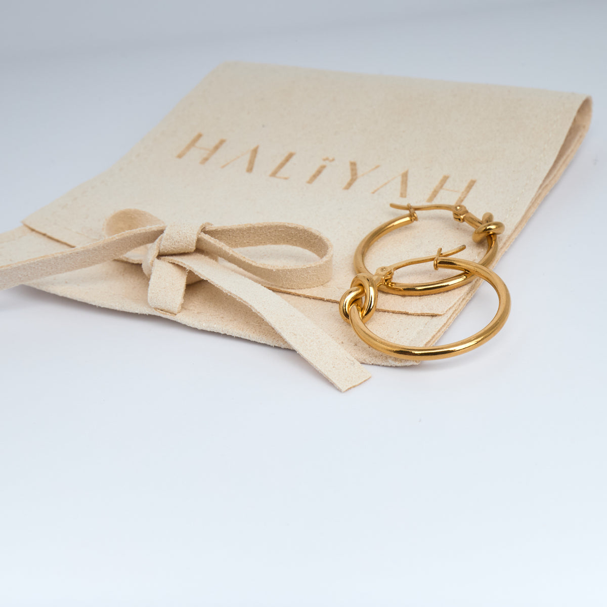 Gold hoop earrings on a beige Haliyah jewelry pouch with a bow.