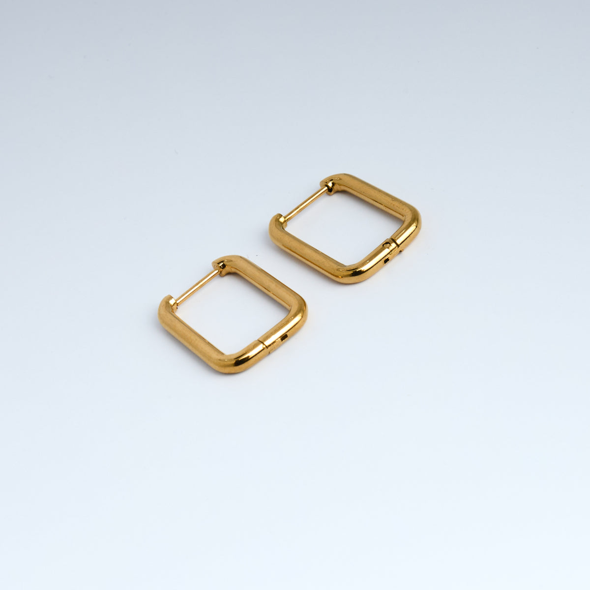 Gold square hoop earrings on a light gray background