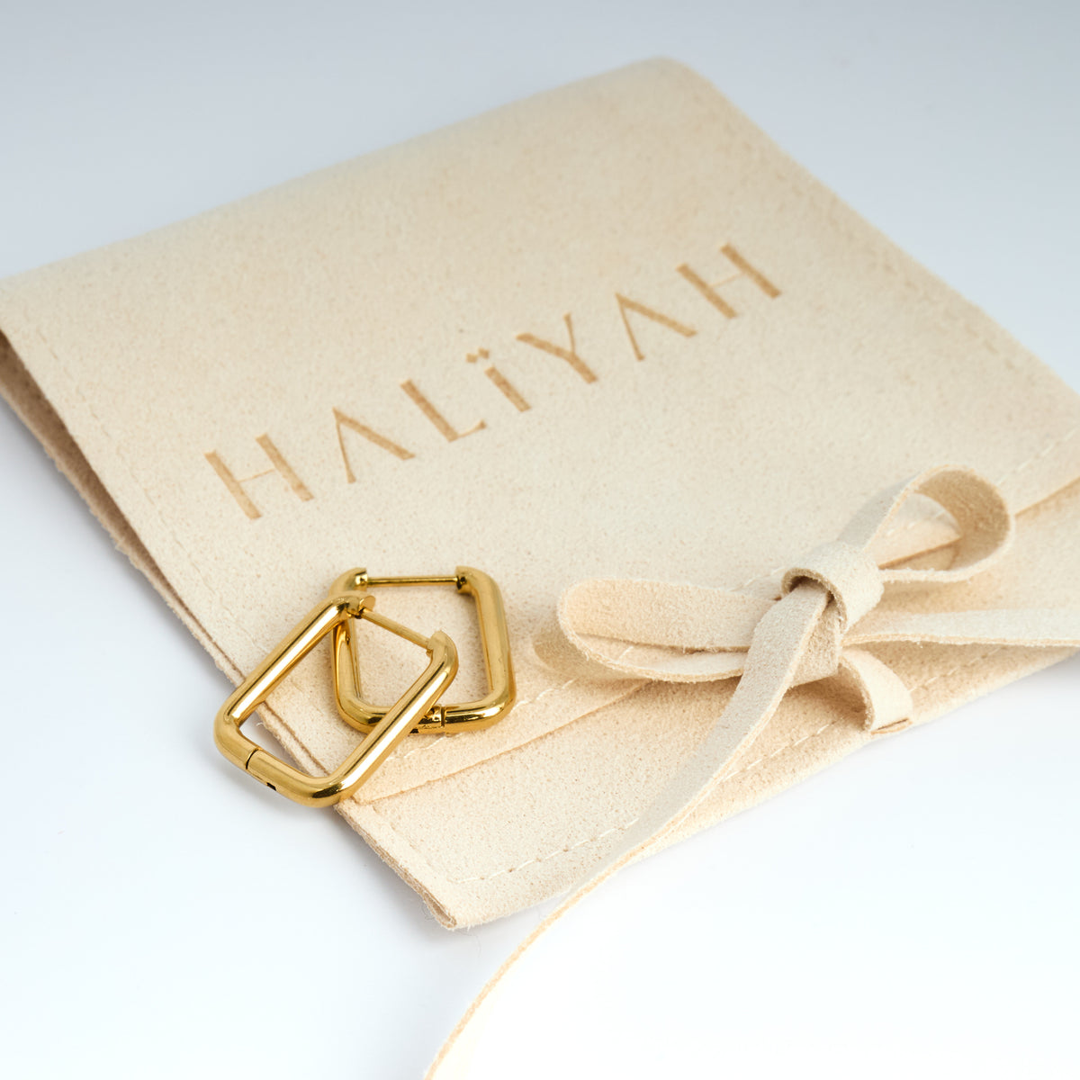 Gold jewellery on a beige pouch with 'HALIYAH' branding on a light grey background