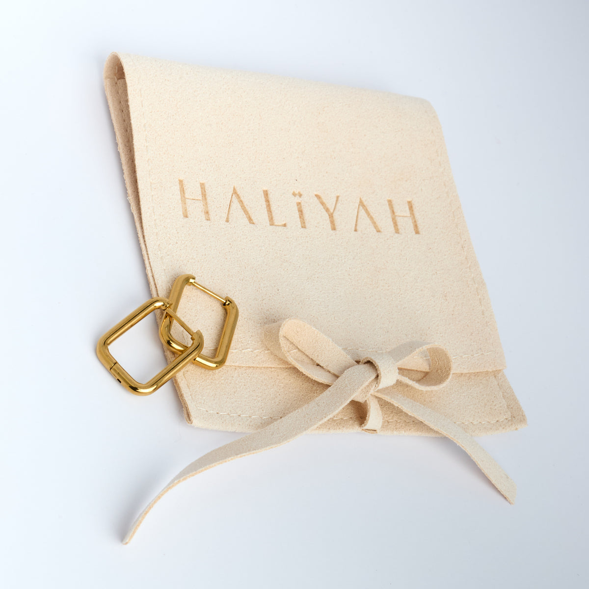 Beige jewellery pouch with gold hoops on a white background, featuring the brand 'HALIYAH'.