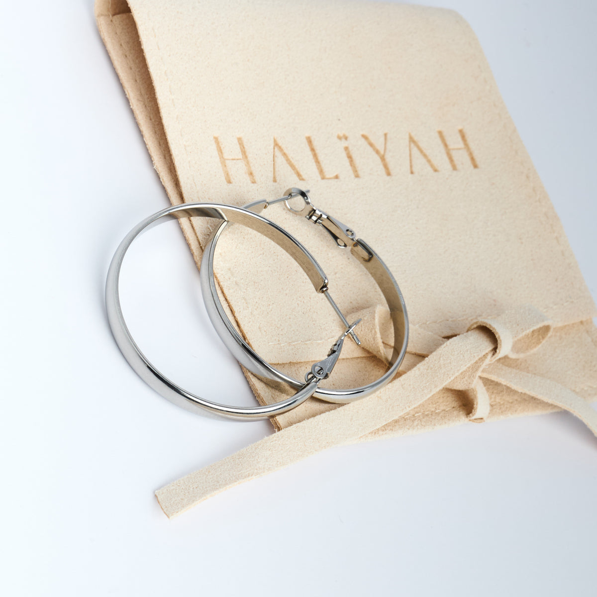 Silver hoop earrings on a beige pouch with 'HALIYAH' branding.