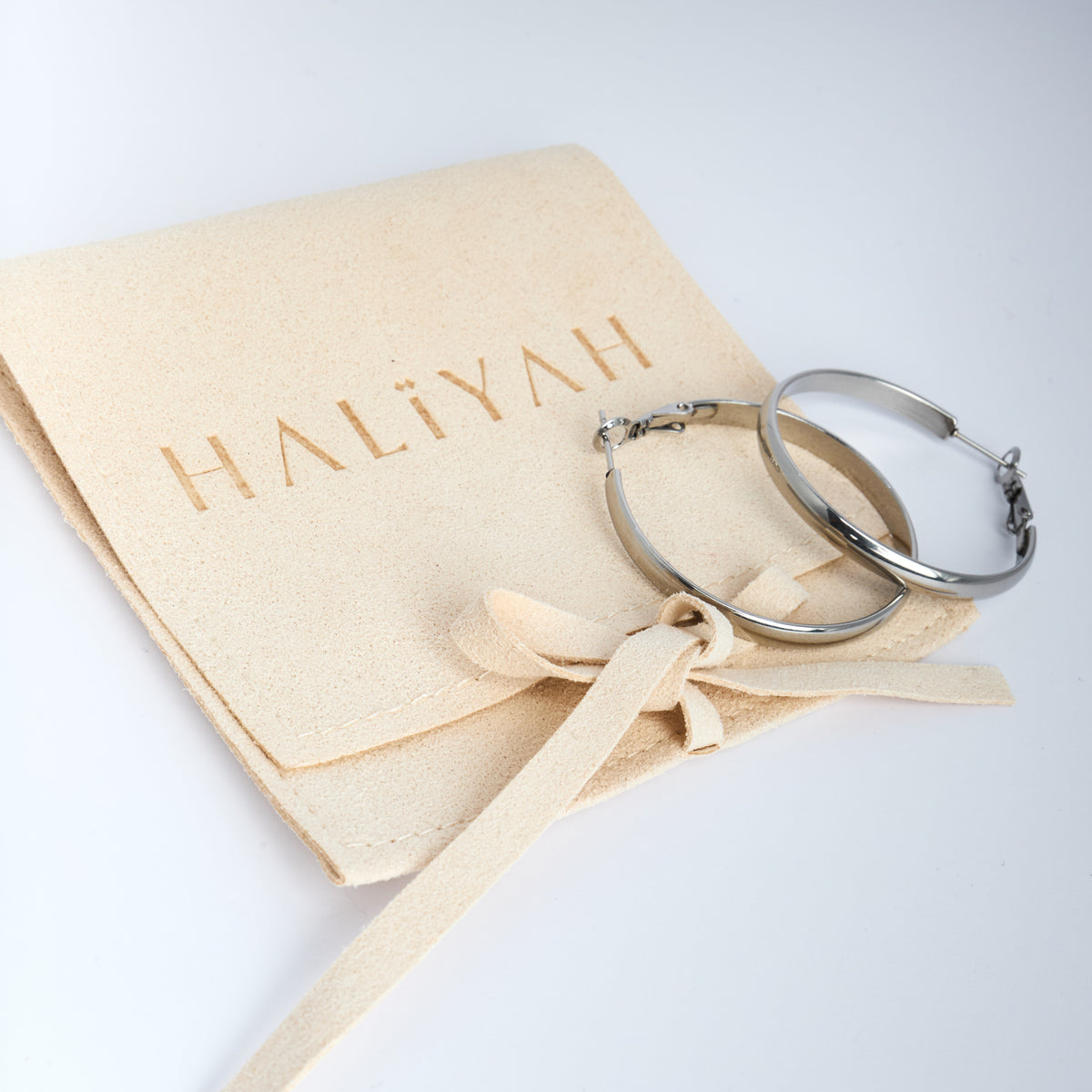 Silver hoop earrings on a Haliyah-branded jewellery pouch with a bow.